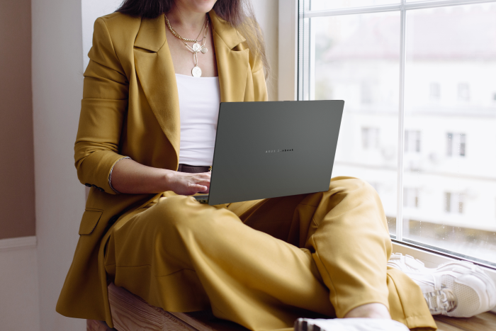 A scenario image of a person in business attire sitting with their legs crossed by a window with an ASUS laptop